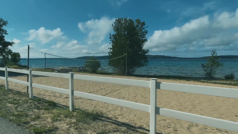 A Sandy Volleyball Court by The Lake, with A White Fence and Clear Skies in The Background